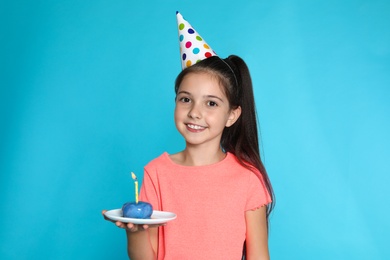 Happy girl holding birthday sweetness with candle on blue background