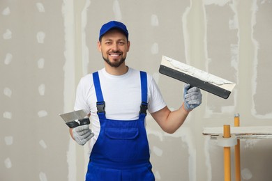 Professional worker with putty knives near wall