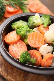 Photo of Mix of different frozen vegetables in bowl on wooden table, closeup