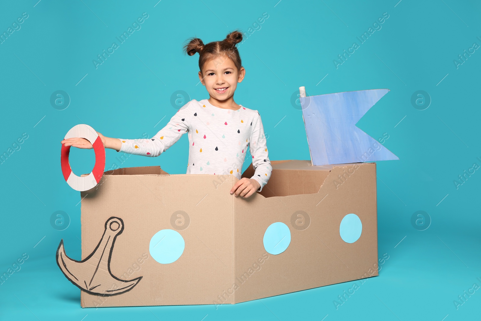 Photo of Cute little girl playing with cardboard boat on color background