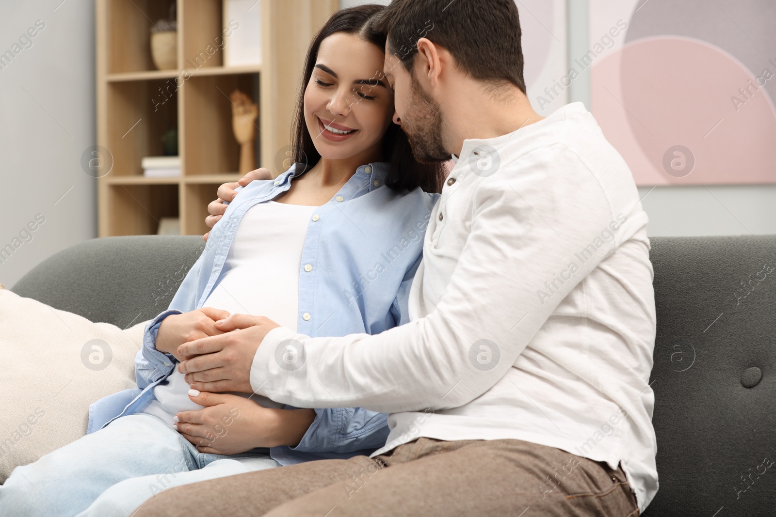 Photo of Happy pregnant woman with her husband on sofa at home