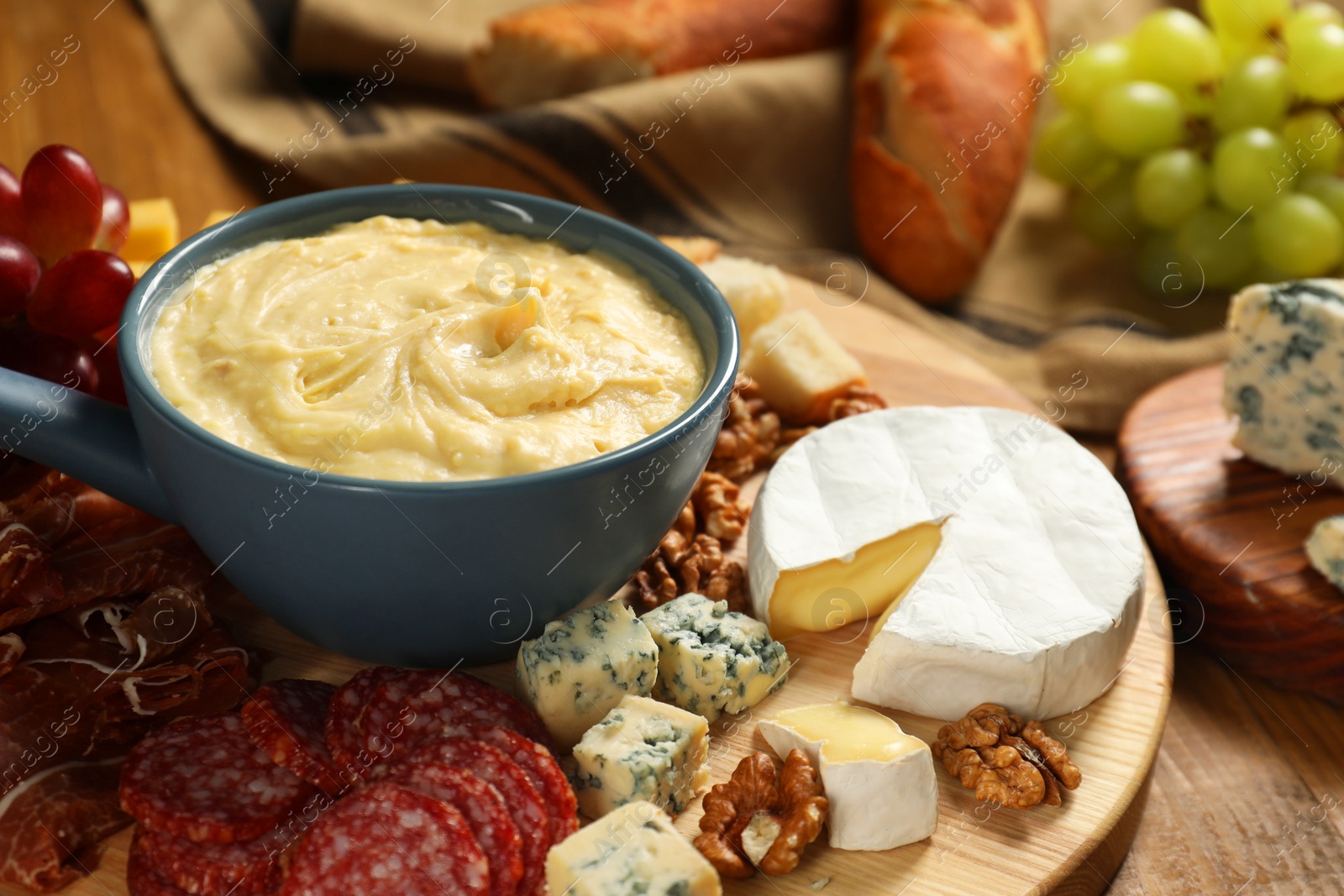 Photo of Fondue pot with tasty melted cheese and different snacks on wooden table