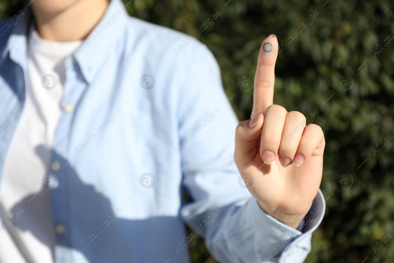 Photo of Woman showing finger with drawn blue circle as World Diabetes Day symbol outdoors, closeup