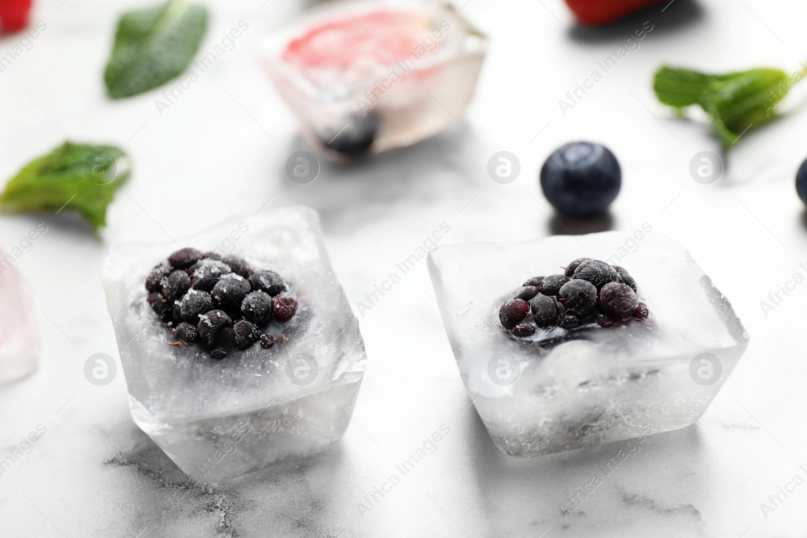 Photo of Ice cubes with blackberries on white marble table, closeup