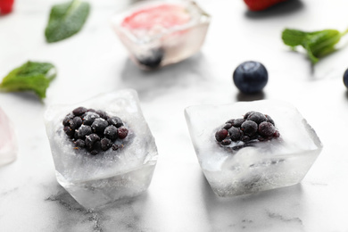 Photo of Ice cubes with blackberries on white marble table, closeup