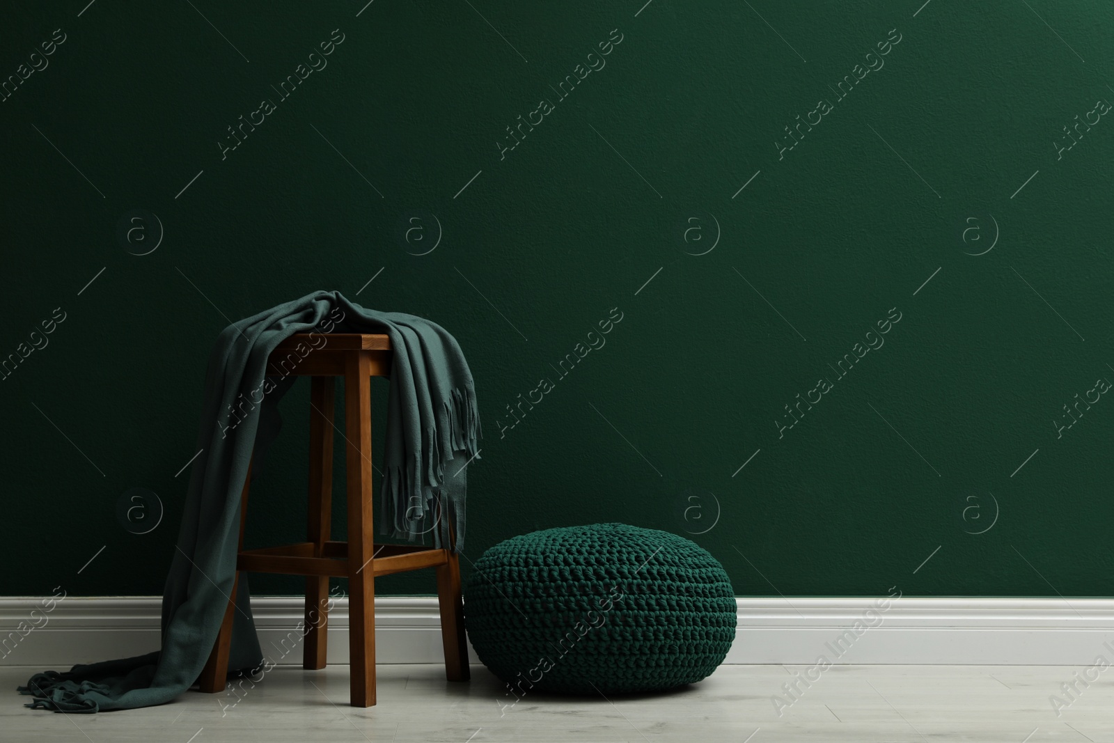 Photo of Stylish knitted pouf and wooden stool with blanket near green wall indoors, space for text