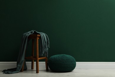 Stylish knitted pouf and wooden stool with blanket near green wall indoors, space for text