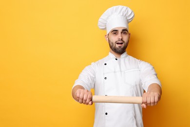 Photo of Professional chef with rolling pin on yellow background. Space for text