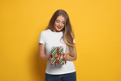 Photo of Emotional young woman holding colorful gift box on yellow background