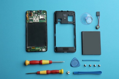 Disassembled mobile phone and repair tools on blue background, flat lay