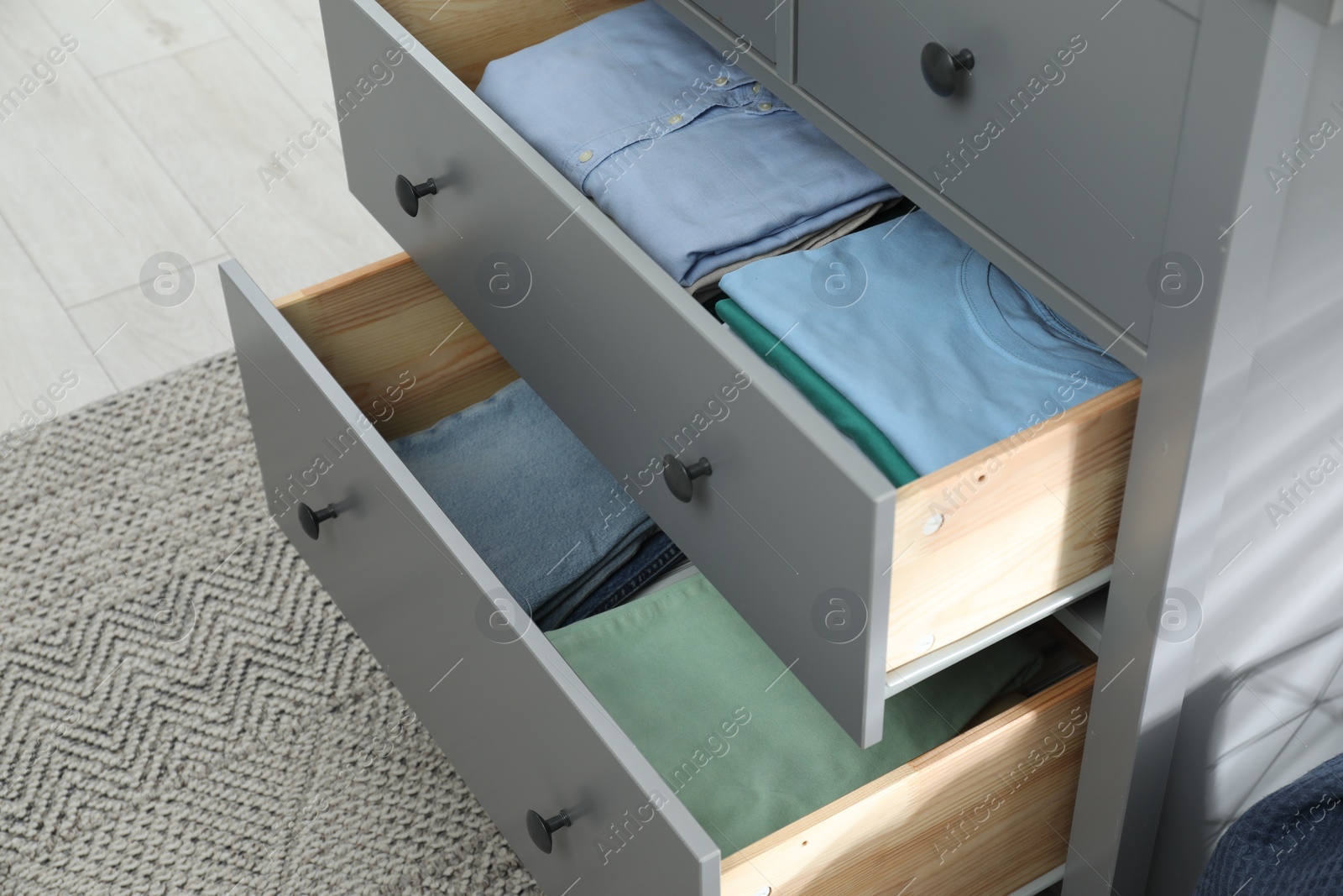 Photo of Sorting and organizing. Chest of drawers with different folded clothes indoors