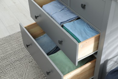 Photo of Sorting and organizing. Chest of drawers with different folded clothes indoors