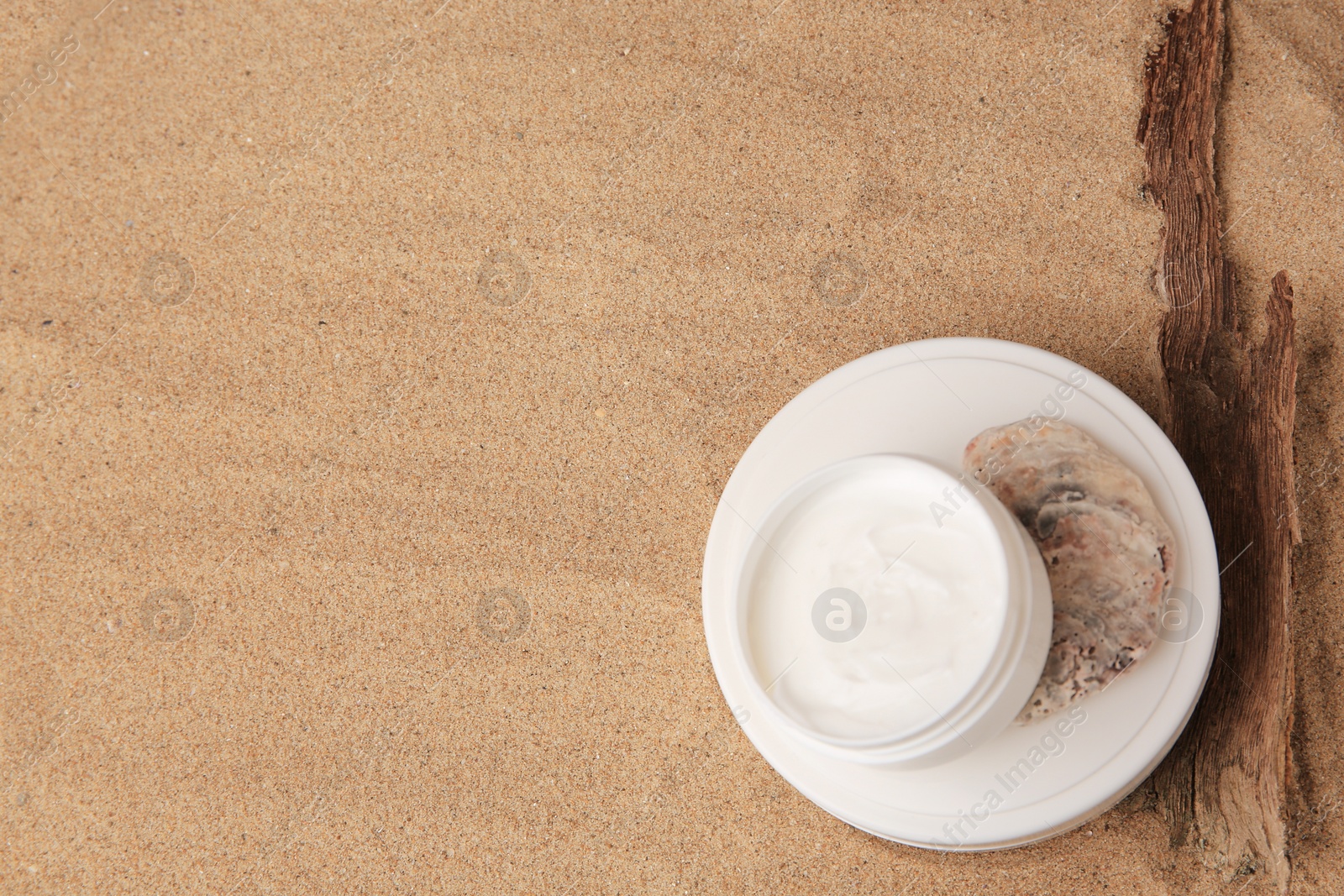 Photo of Jar of cream, stone and tree bark on sand, flat lay. Space for text