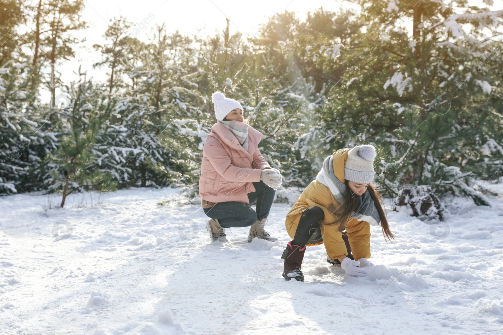 Photo of Mother and daughter rolling snowballs in winter forest