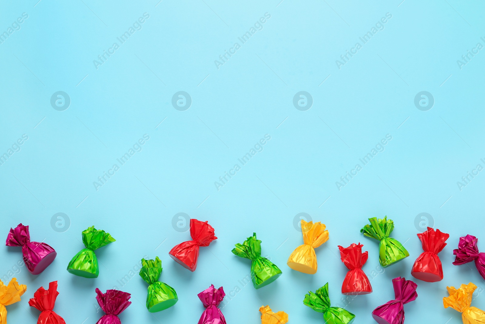 Photo of Candies in colorful wrappers on light blue background, flat lay. Space for text