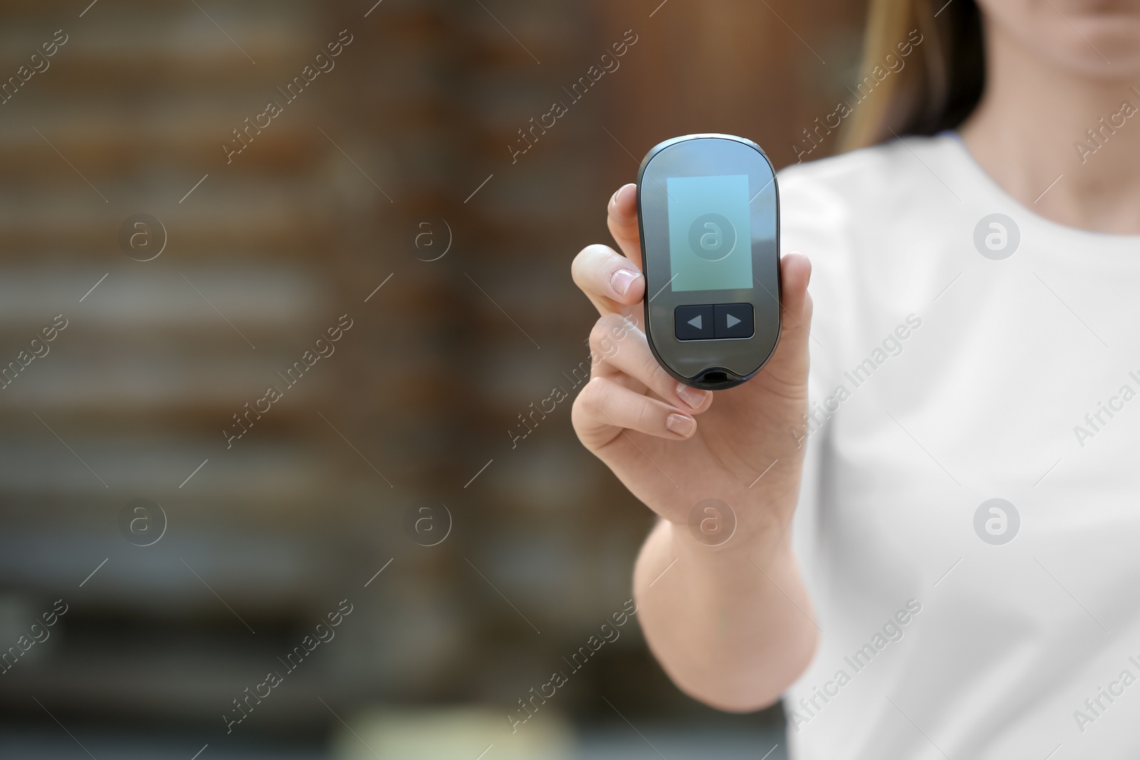 Photo of Woman holding digital glucometer on blurred background. Diabetes control