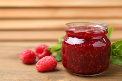 Photo of Delicious jam and fresh raspberries on wooden table, closeup. Space for text