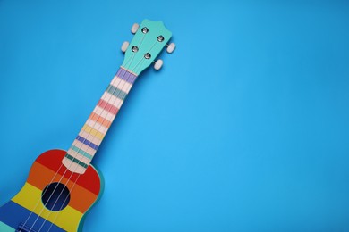 Photo of Colorful ukulele on light blue background, top view and space for text. String musical instrument