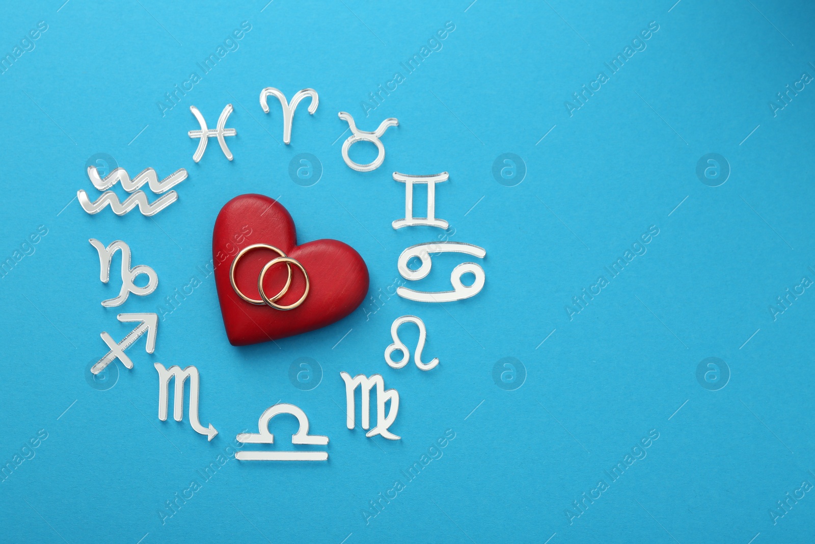 Photo of Zodiac signs, heart and wedding rings on light blue background, flat lay. Space for text