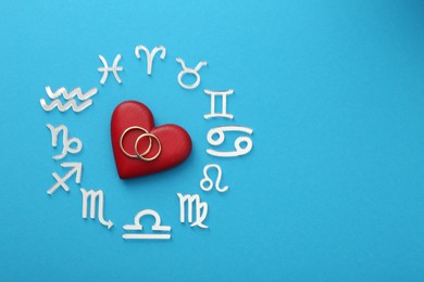 Photo of Zodiac signs, heart and wedding rings on light blue background, flat lay. Space for text