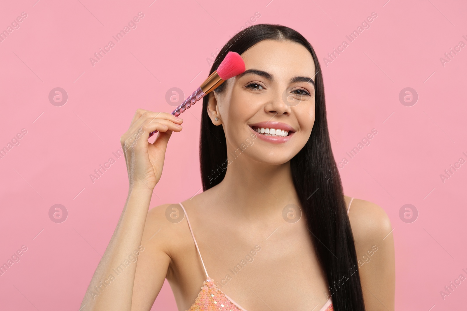 Photo of Beautiful woman applying makeup with brush on pink background