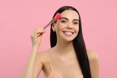 Photo of Beautiful woman applying makeup with brush on pink background