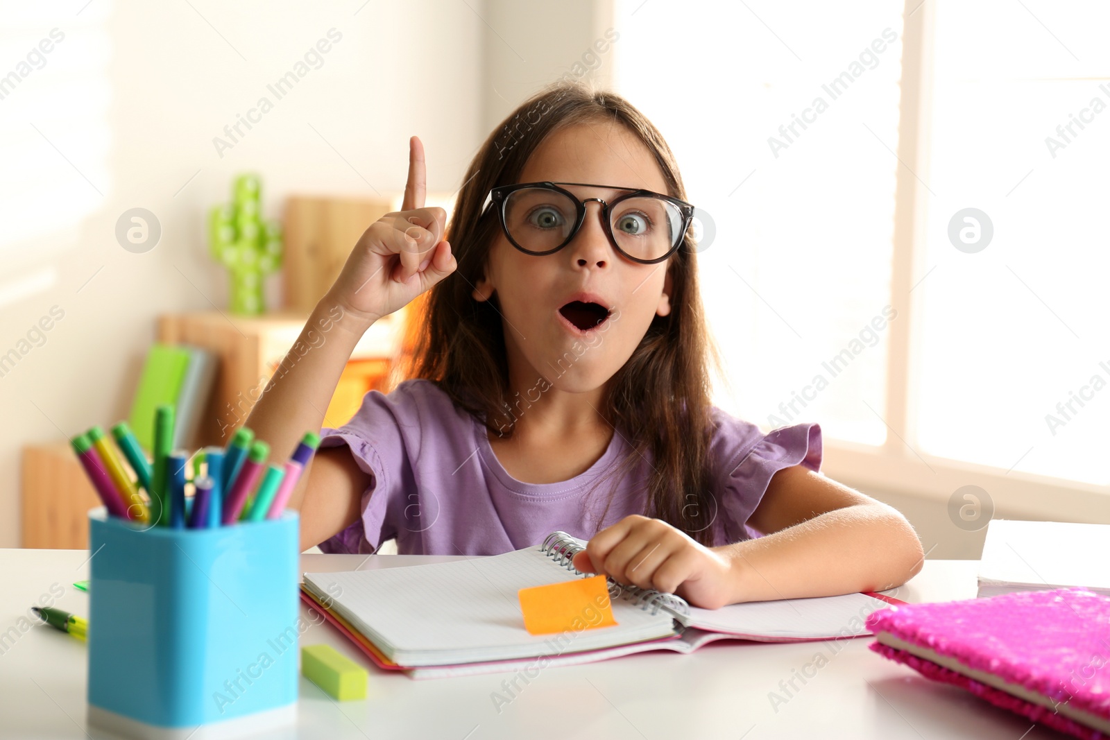 Photo of Emotional little girl doing homework at table indoors