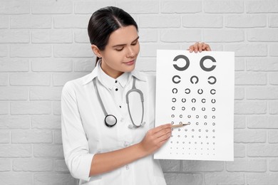 Ophthalmologist pointing at vision test chart near white brick wall