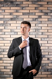 Handsome young man in suit near brick wall background