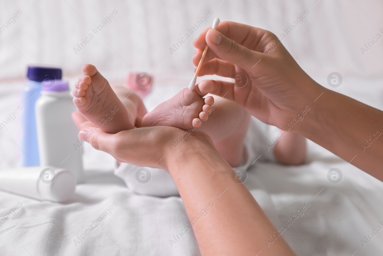 Photo of Mother cleaning baby's foot with cotton bud on bed, closeup