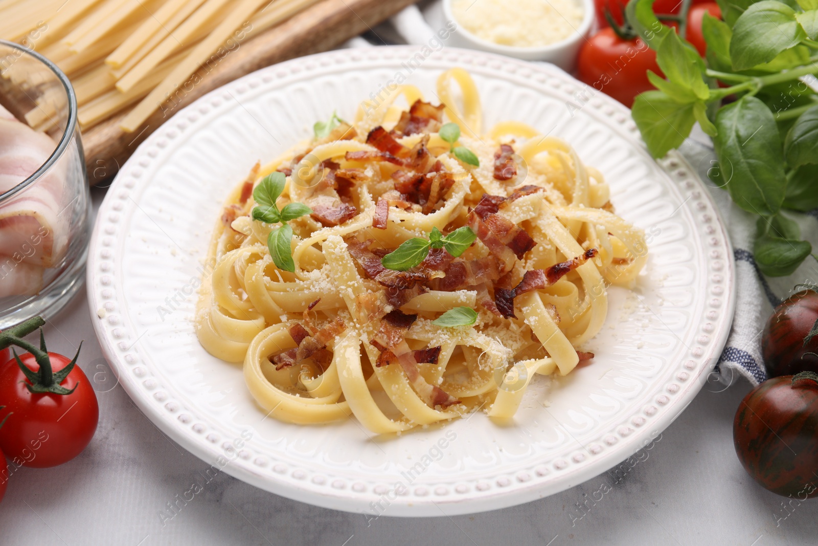 Photo of Tasty pasta with bacon and basil on white marble table