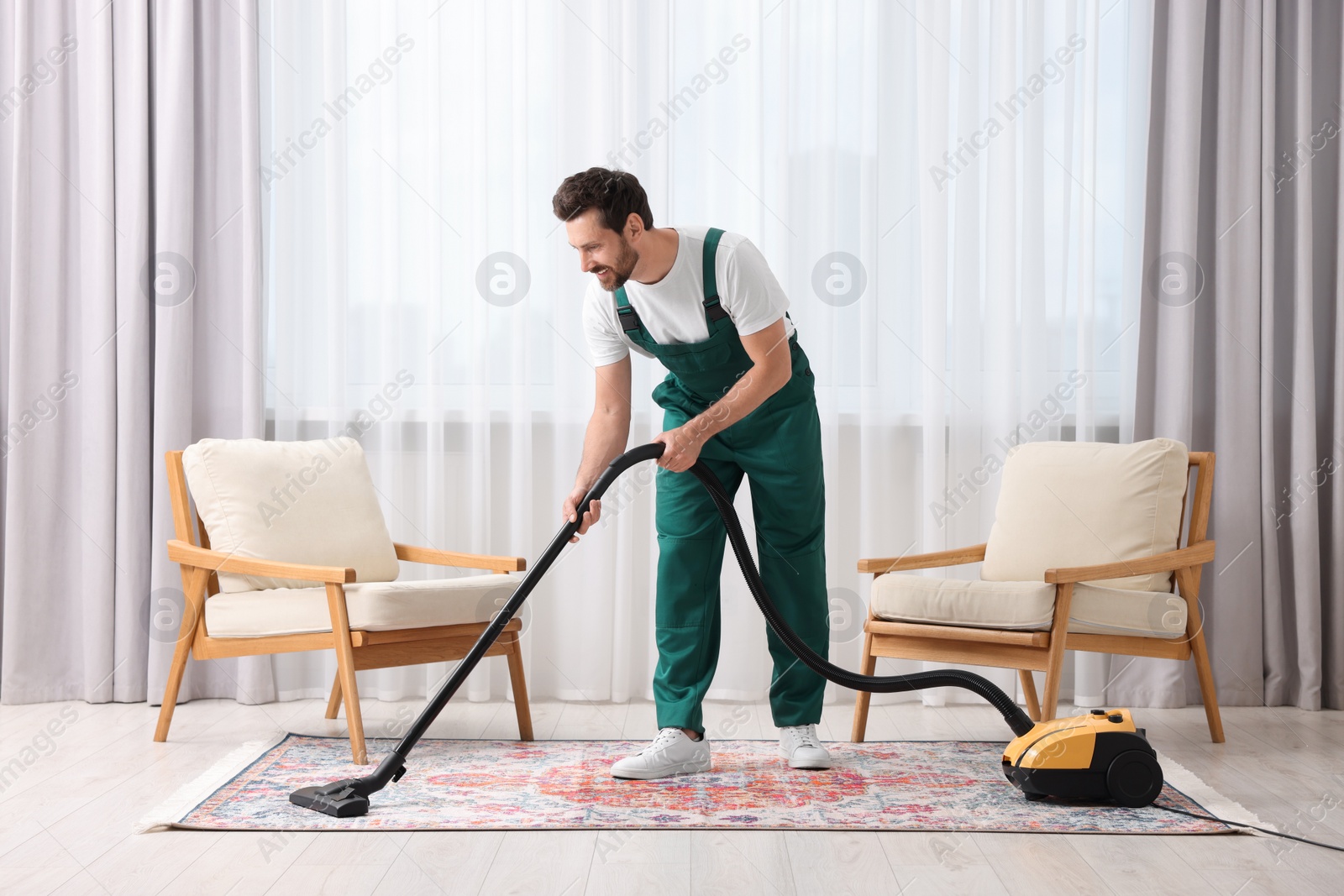 Photo of Dry cleaner's employee hoovering carpet with vacuum cleaner in room