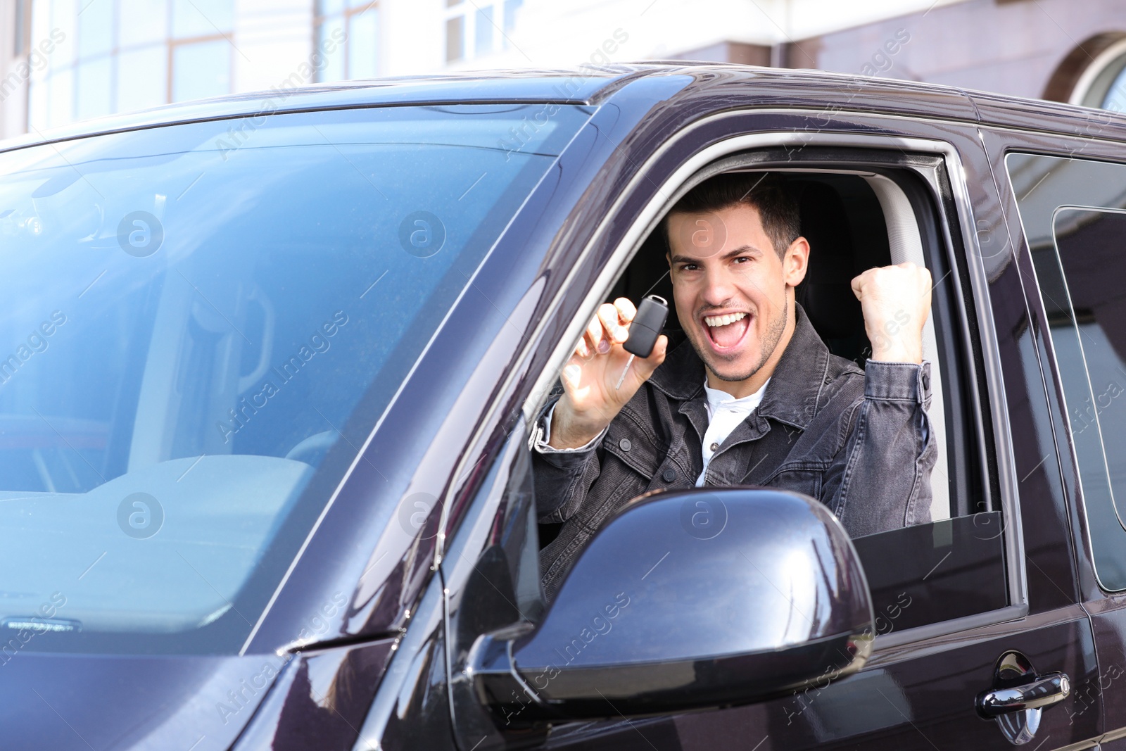 Photo of Excited man with key sitting in car outdoors. Buying new auto