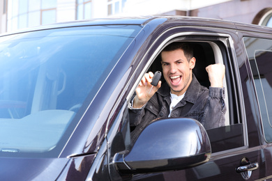 Photo of Excited man with key sitting in car outdoors. Buying new auto