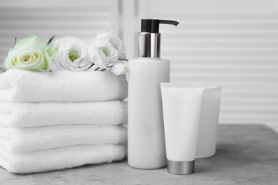 Photo of Towels, cosmetic products and flowers on grey table indoors