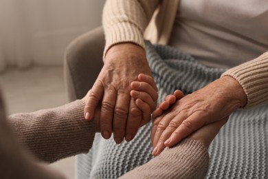 Photo of Young and elderly women holding hands together indoors, closeup