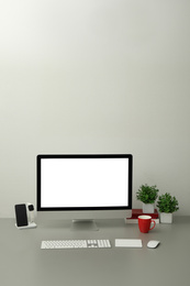 Photo of Modern workplace with computer, charging devices and houseplants. Interior design