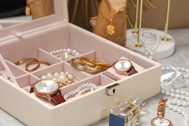 Photo of Jewelry box with many different accessories and perfume on light grey table, closeup