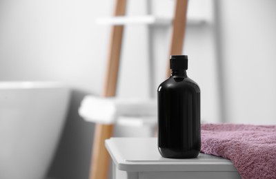 Photo of Bottle of bubble bath and towel on white table in bathroom, space for text