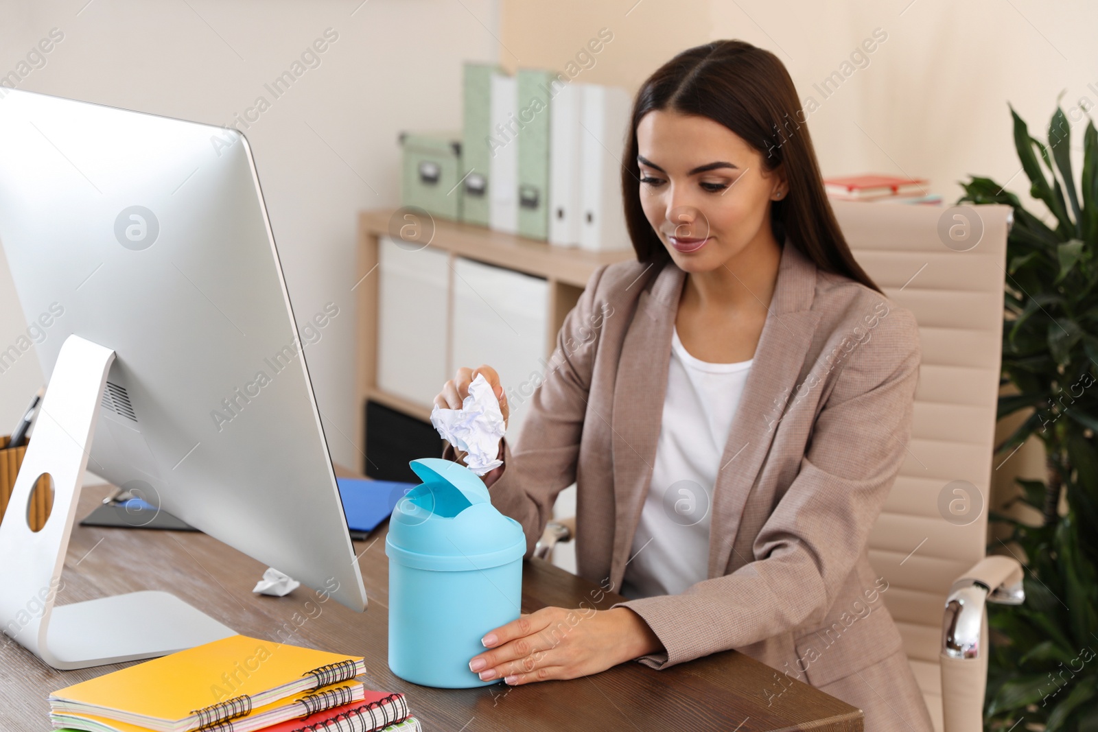 Photo of Young woman throwing paper into recycling bin at office