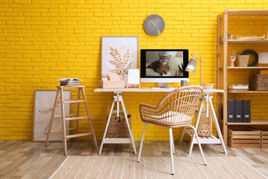 Stylish home office interior with comfortable workplace near yellow brick wall