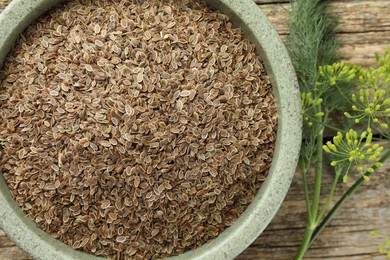 Dry seeds and fresh dill on wooden table, flat lay