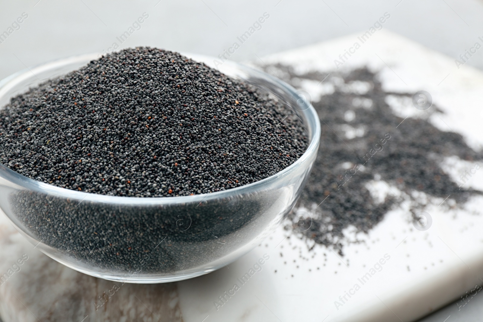 Photo of Poppy seeds in bowl on white marble board, closeup