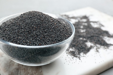 Poppy seeds in bowl on white marble board, closeup