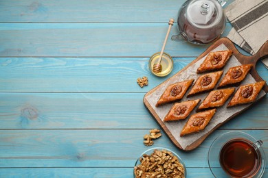 Photo of Delicious sweet baklava with walnuts, honey and hot tea on turquoise wooden table, flat lay. Space for text