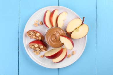 Photo of Fresh red apple with peanut butter and nuts on light blue wooden table, top view