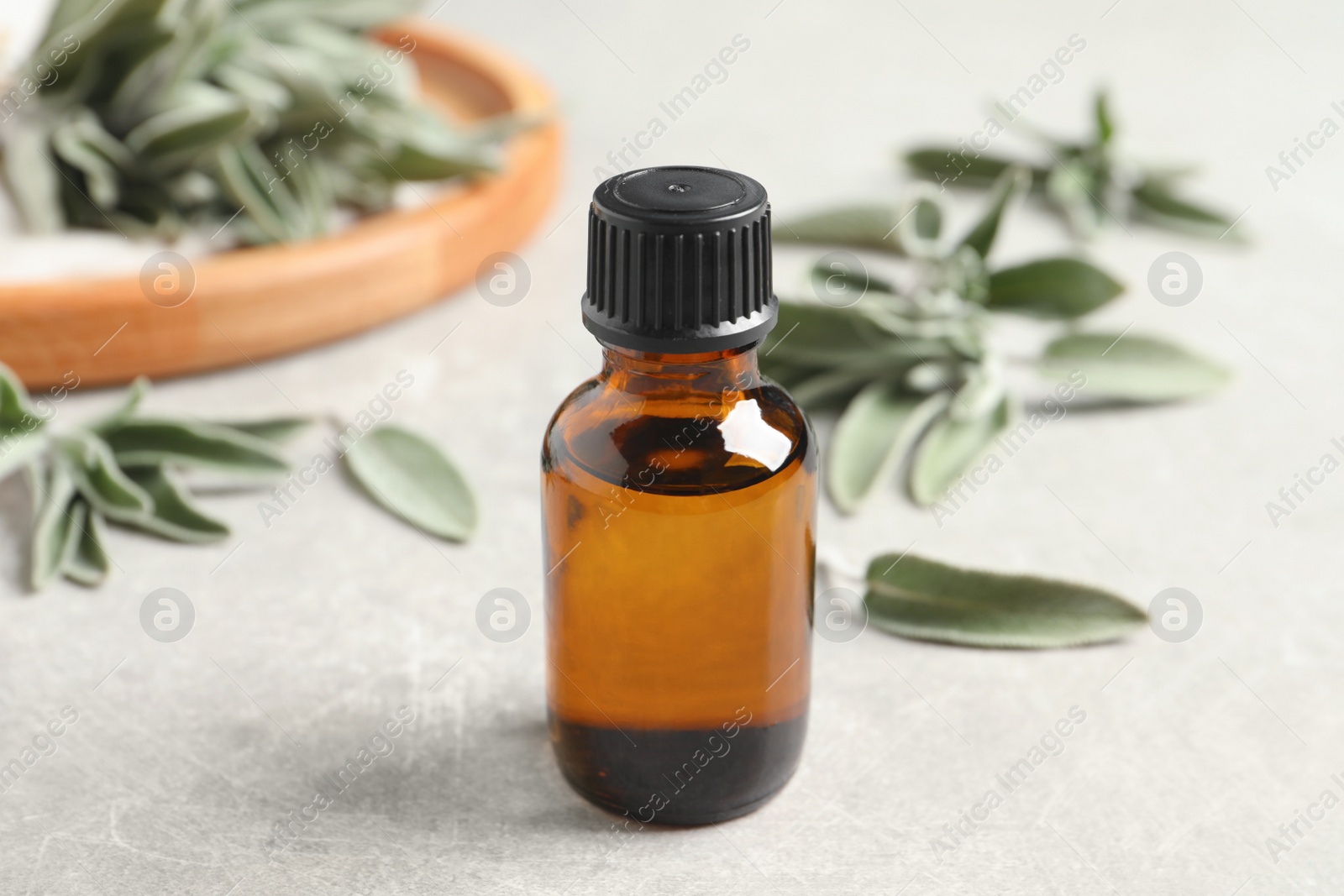 Photo of Bottle of essential sage oil and leaves on light grey table