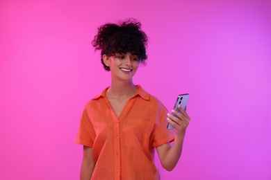 Happy woman sending message via smartphone on color background