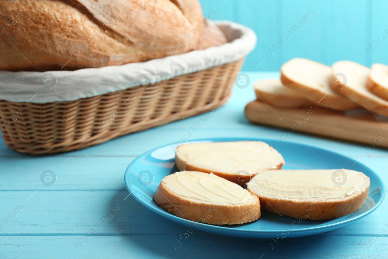 Photo of Slices of tasty fresh bread with butter on light blue wooden table