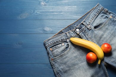 Photo of Men jeans, banana and nectarines symbolizing male genitals on blue wooden table, top view with space for text. Potency concept